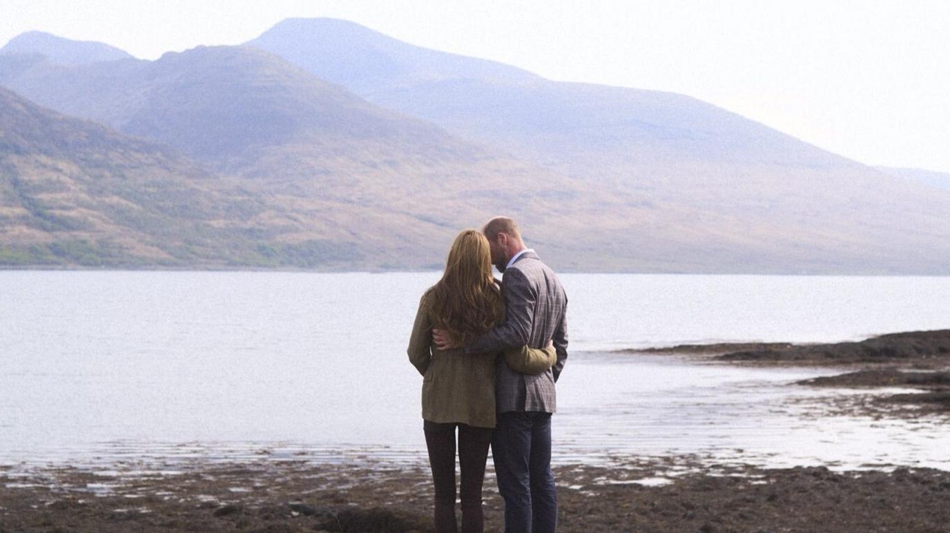 The royal couple on the Isle of Mull, pictured from behind. They have one arm around each other's waists and appear to be talking