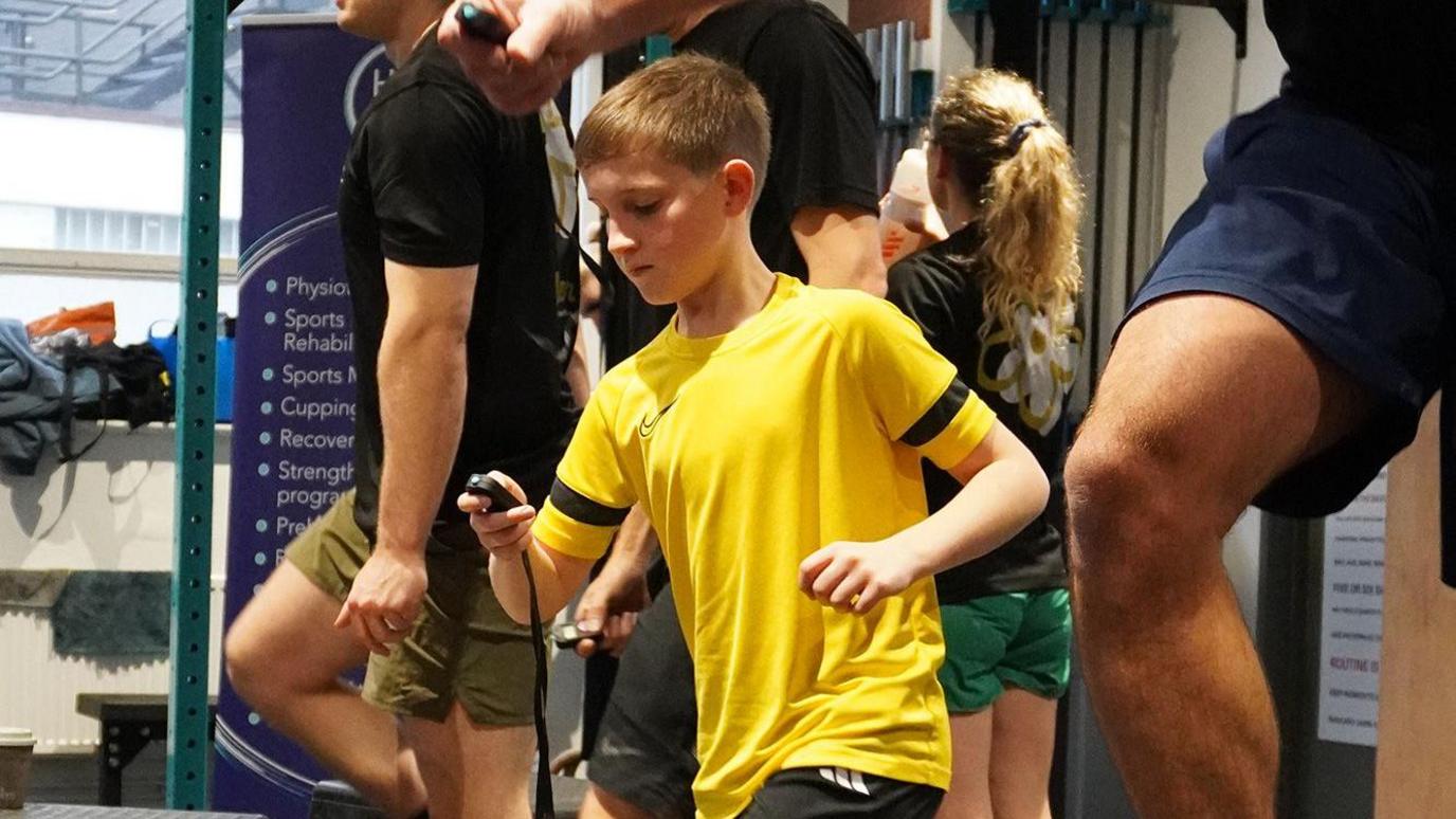 Ten-year-old Joe is box stepping. He is wearing a yellow T-shirt and is looking at a stopwatch.