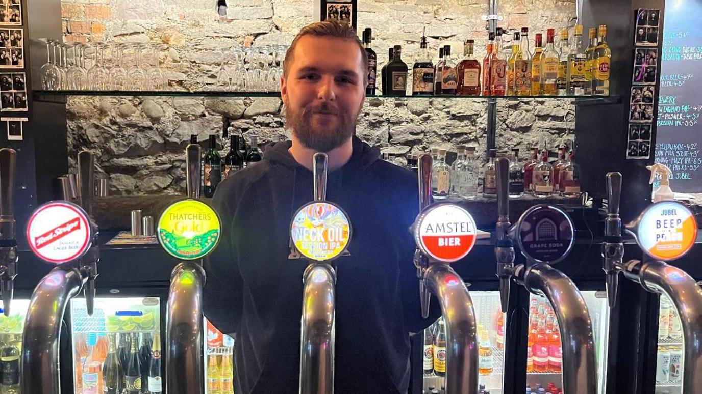 Callum De-Ritter standing behind the bar at Kongs with several beer taps in front of him