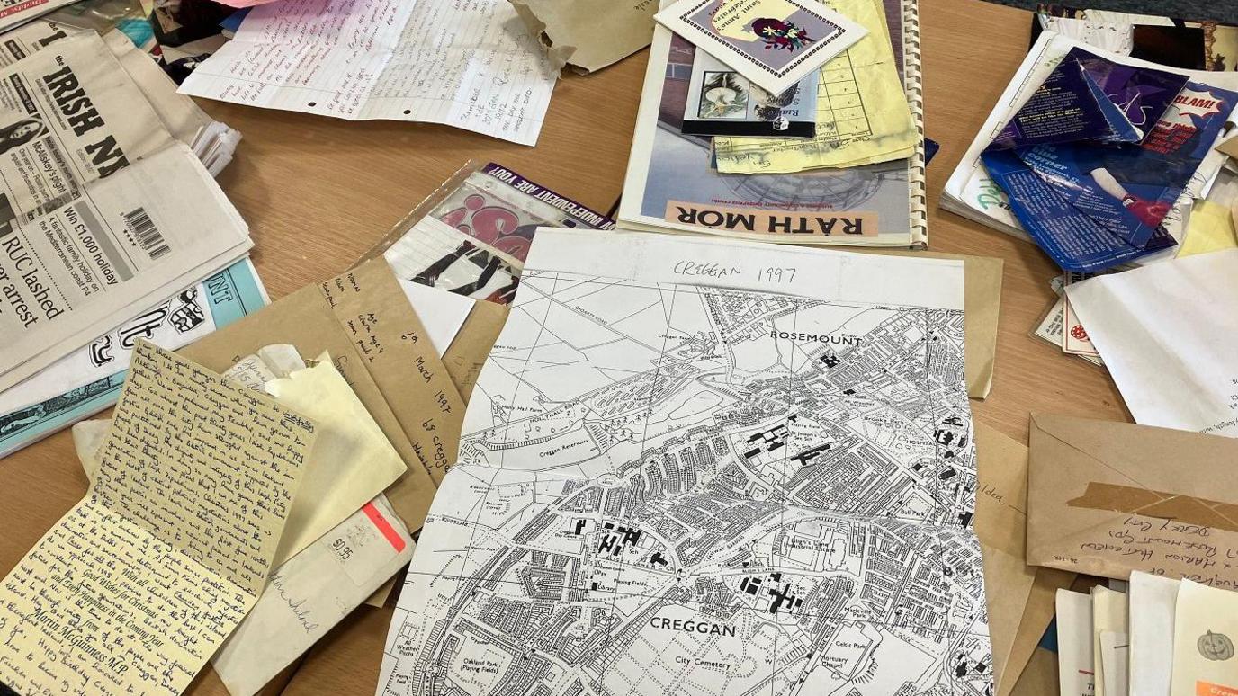 A number of artefacts, including a map, and handwritten letters are laid out on a table after being taken out of a time capsule