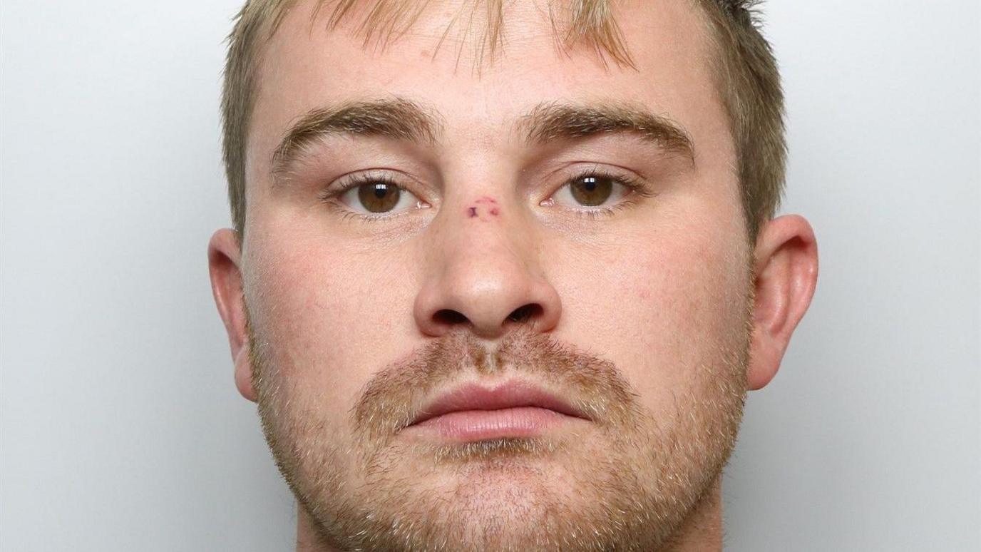 A custody image of a young man with light hair and facial stubble.