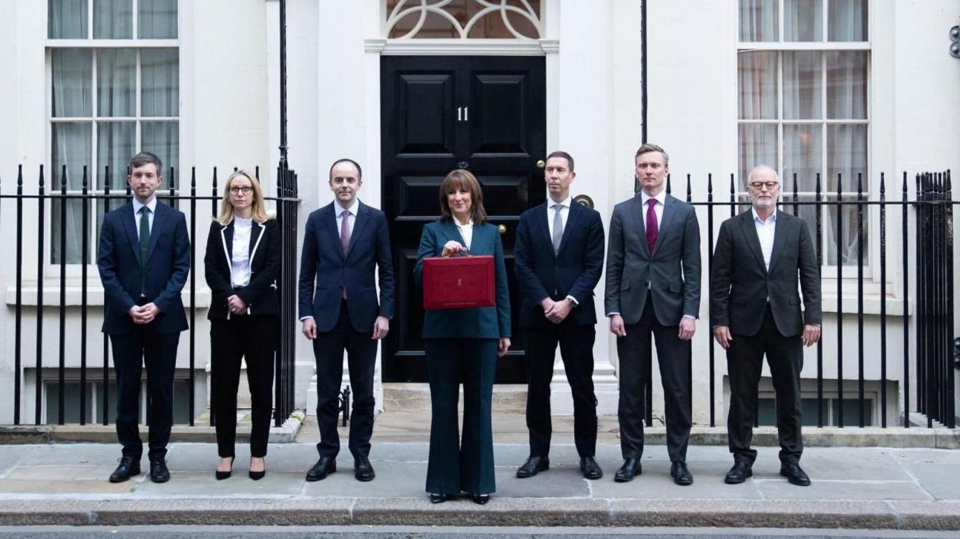 Reeves, standing alongside her economic aides, holds a red briefcase up in front of the door of No 11 Downing Street.