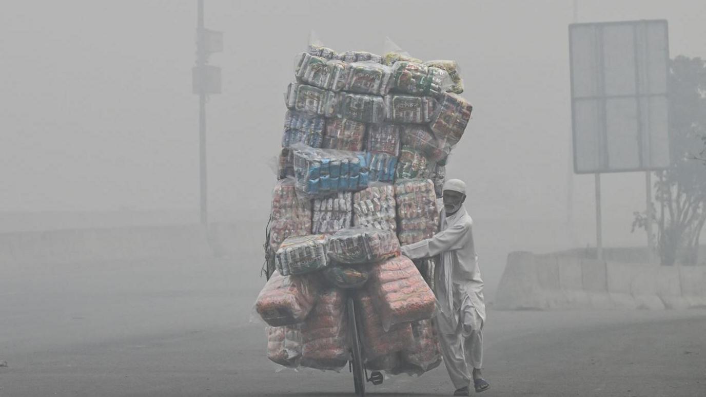 A vendor transports food items on his bicycle cart along a road engulfed in smog in Lahore 