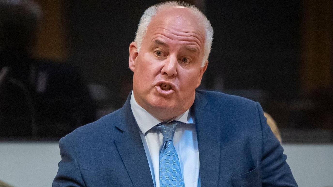 Andrew RT Davies speaking in the Senedd chamber wearing a blue suit, shirt and tie