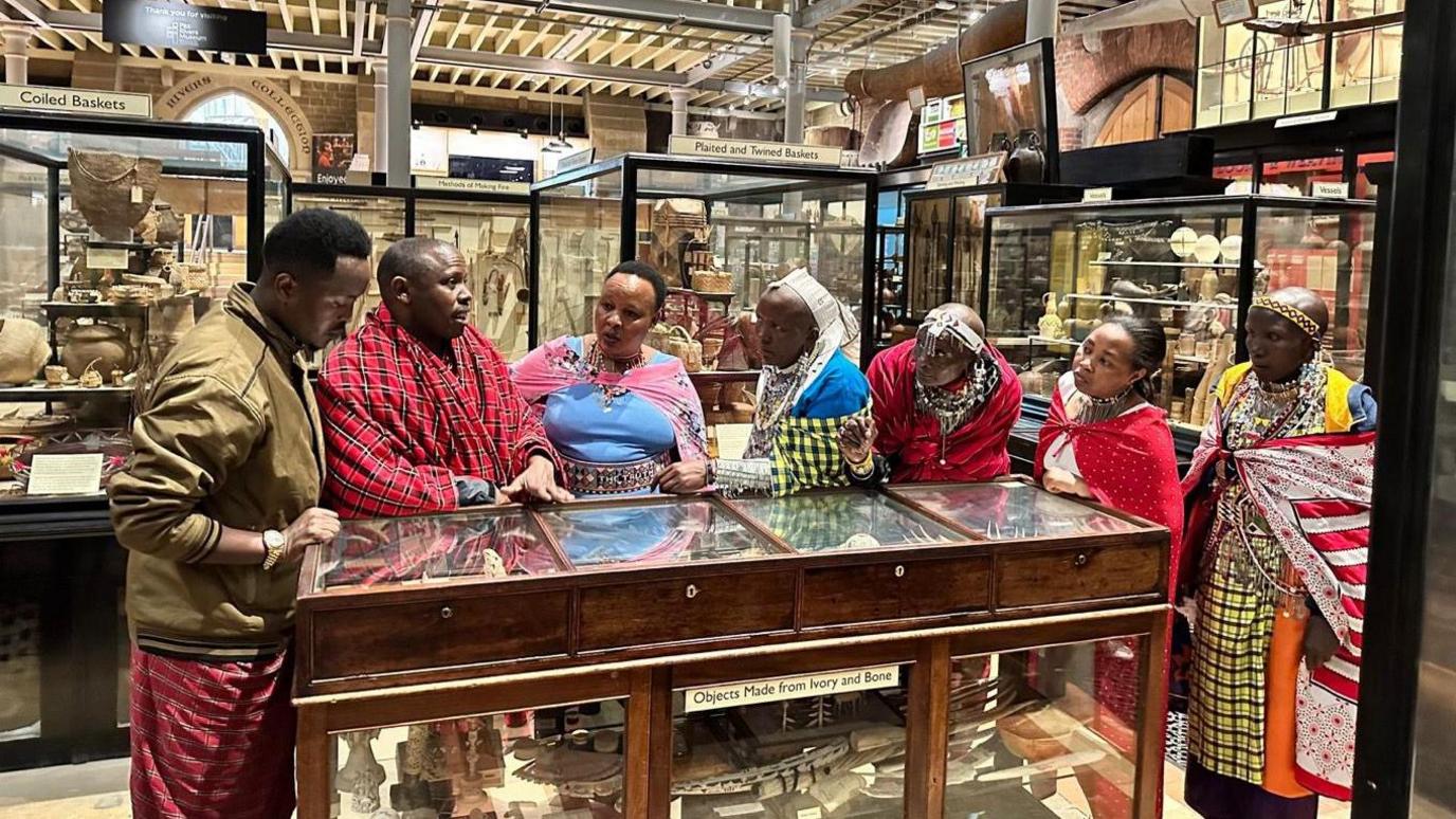 A group of Maasai people crowded around a display cabinet at the Pitt Rivers Museum.