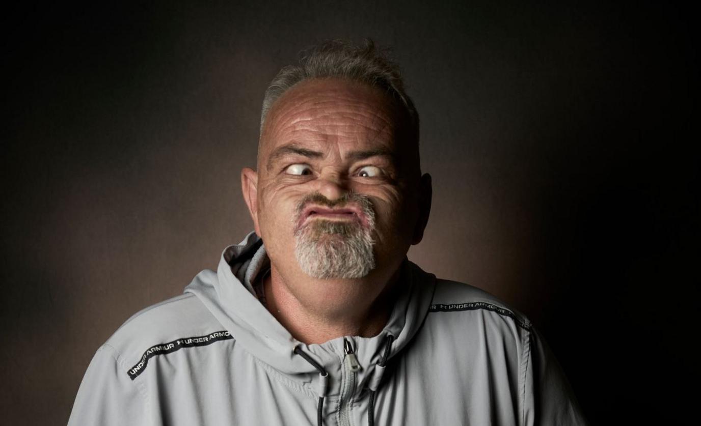 Ged Eccles, who has short grey hair and a goatee, pushes his mouth up beneath his nose with his cheeks raised and his eyes crossed