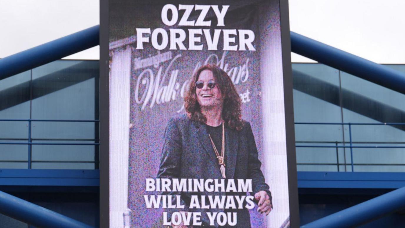 A board that has a picture of Ozzy Osbourne on it. It reads "Ozzy forever, Birmingham will always love you"