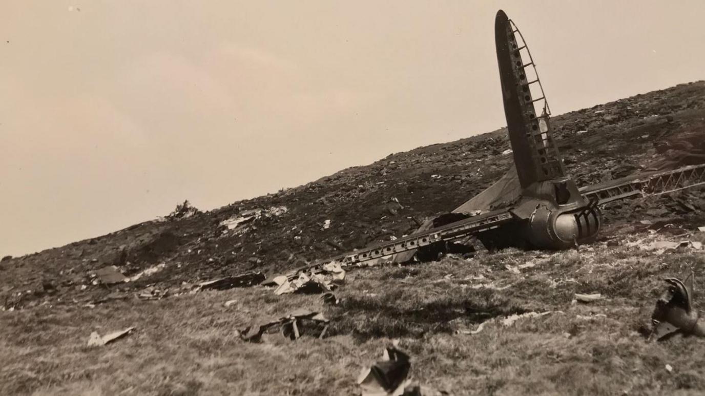 The tail end of the Dottie Jeanne surrounded by wreckage on a hillside. Photo is in sepia colours.