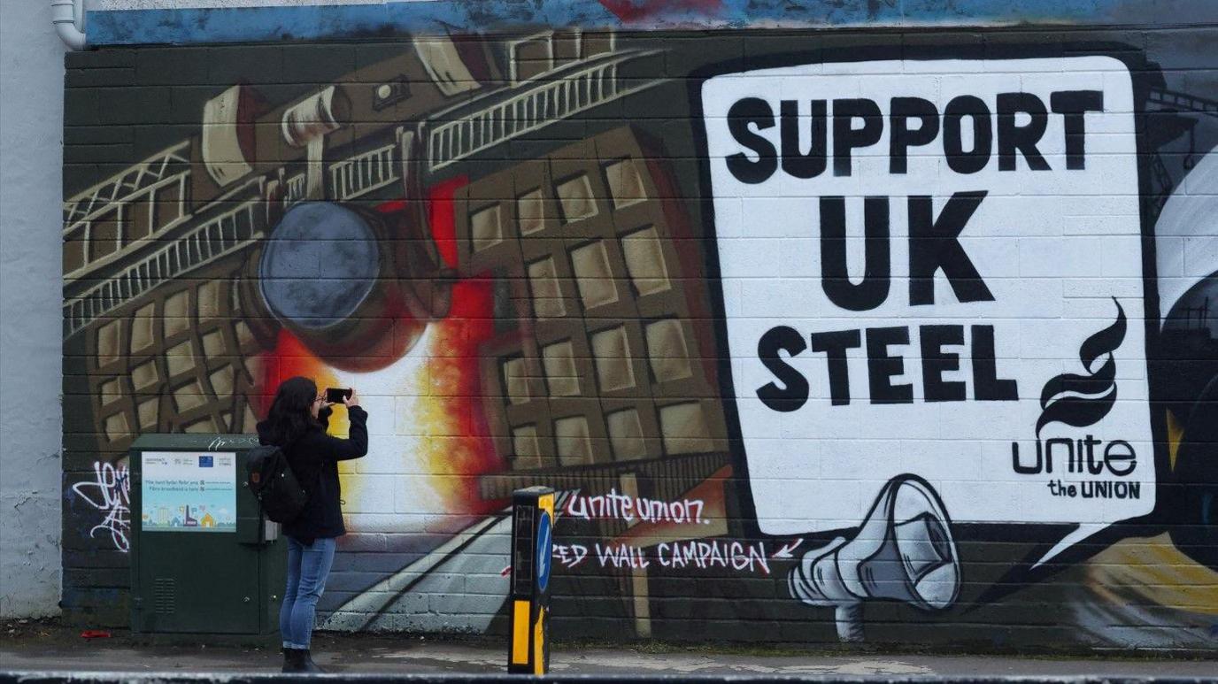 A woman photographs a mural by the Unite union which reads Support UK Steel