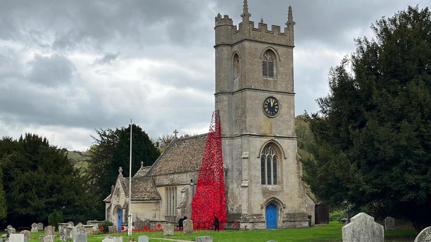 A bright red display of red poppies can be seen draped onto the side of a church, spilling onto the lawn by a graveyard.