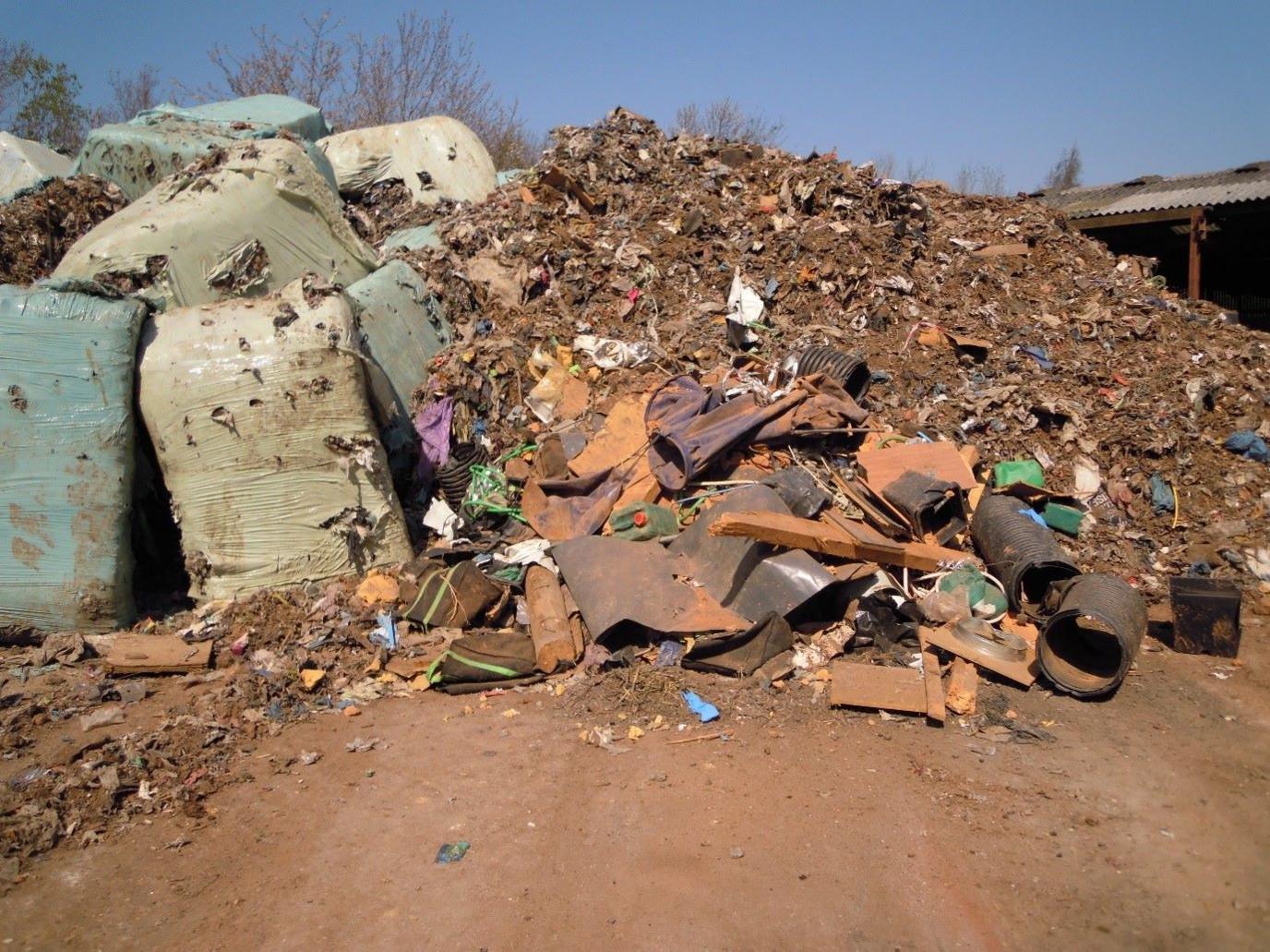 A pile of decomposing waste which had been dumped at a site in Lincolnshire. Blue bales are stacked at the left of the image but have partially split. A large mound of brown-coloured rubbish, including what looks like pieces of metal, is visible on the right of the image.