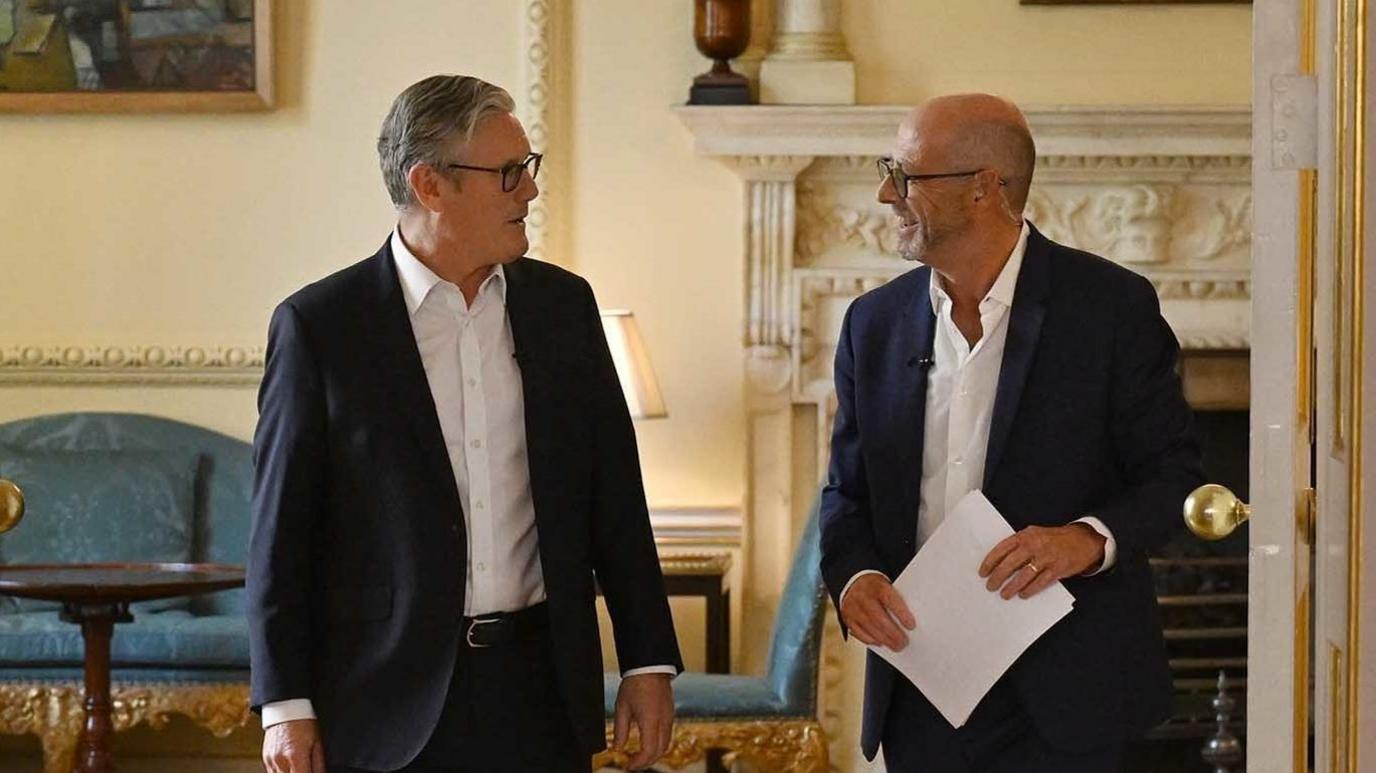 Two men (Sir Keir Starmer and Nick Robinson) look at each other as they walk through a doorway