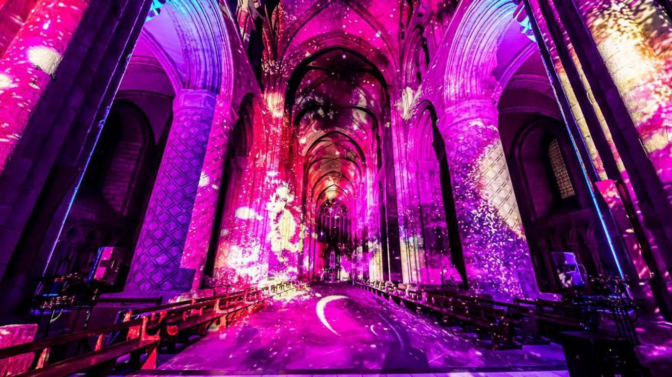 Pink, purple and red projections on the interior of Durham Cathedral. A yellow moon crescent is projected on the floor.