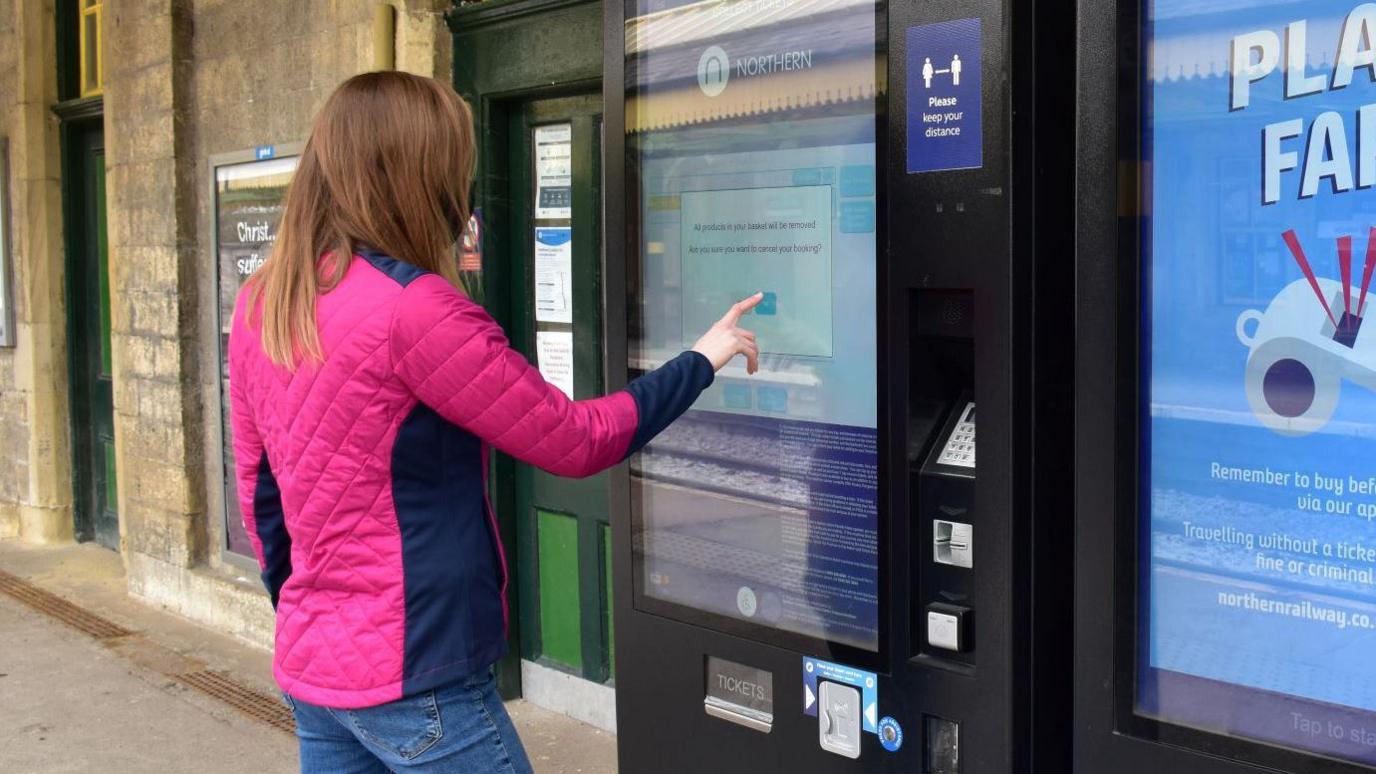 A women in a pink jacket buys a ticket from a Northern ticket machine