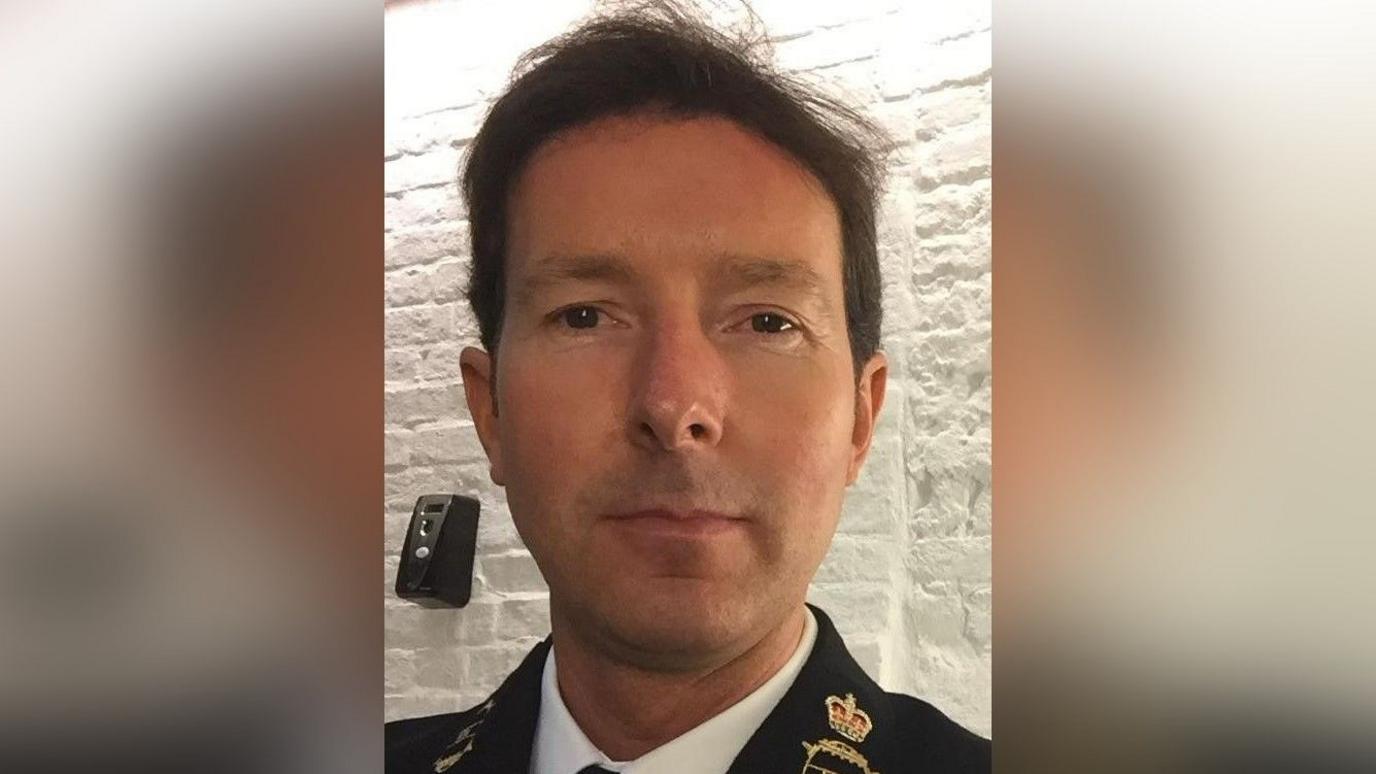 Dyn gyda gwallt brown yn edrych at y camera.