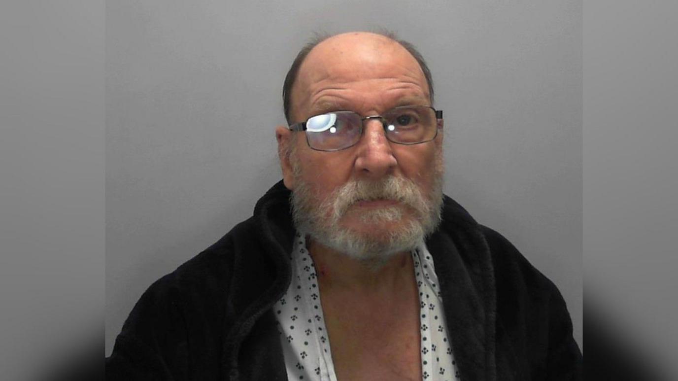 An older man wearing glasses and a dressing gown over a pajama top