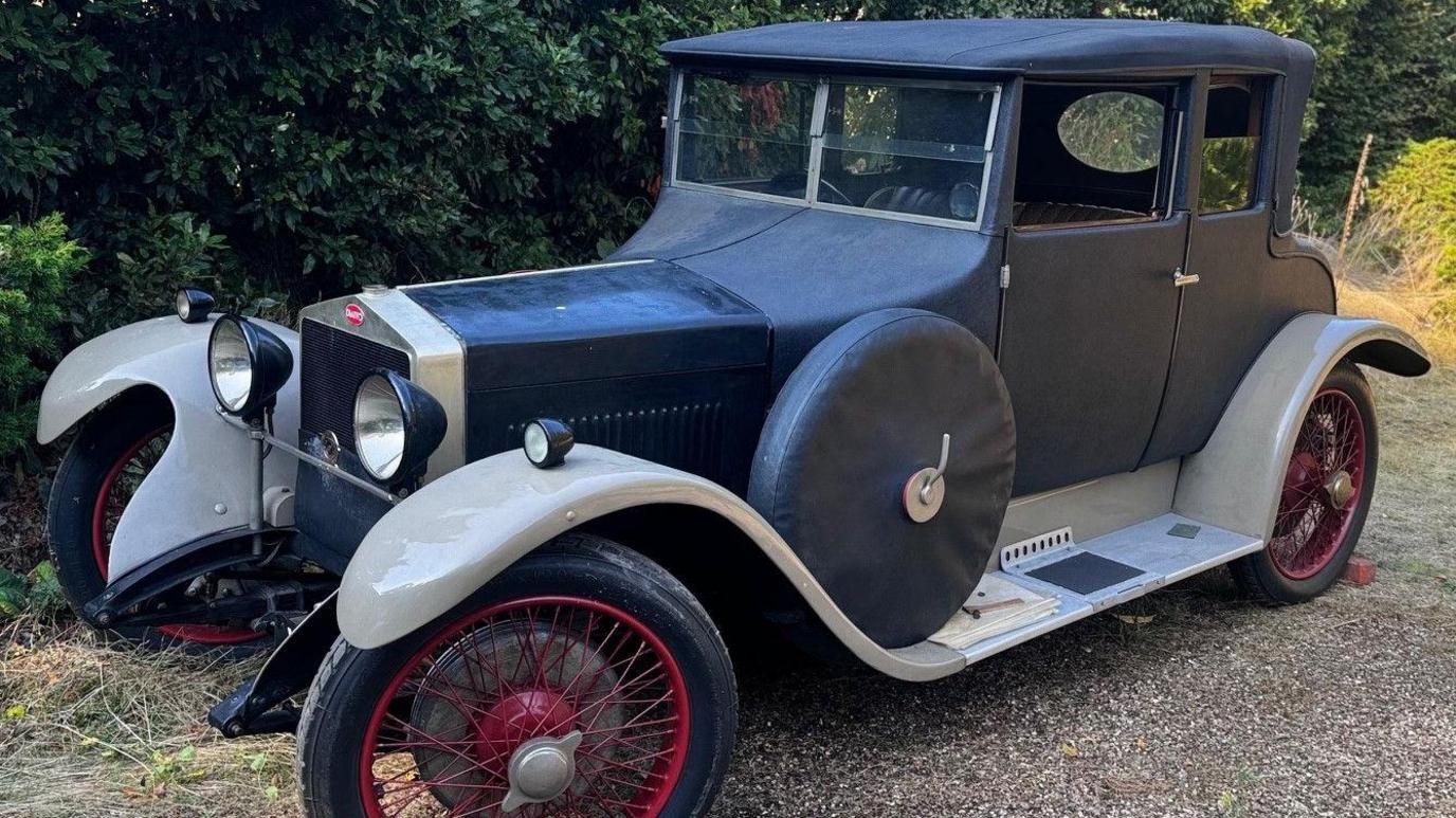 A black 1927 Diatto Type 30 car, which has red spokes on its wheels. While the main body is black, its base is cream.