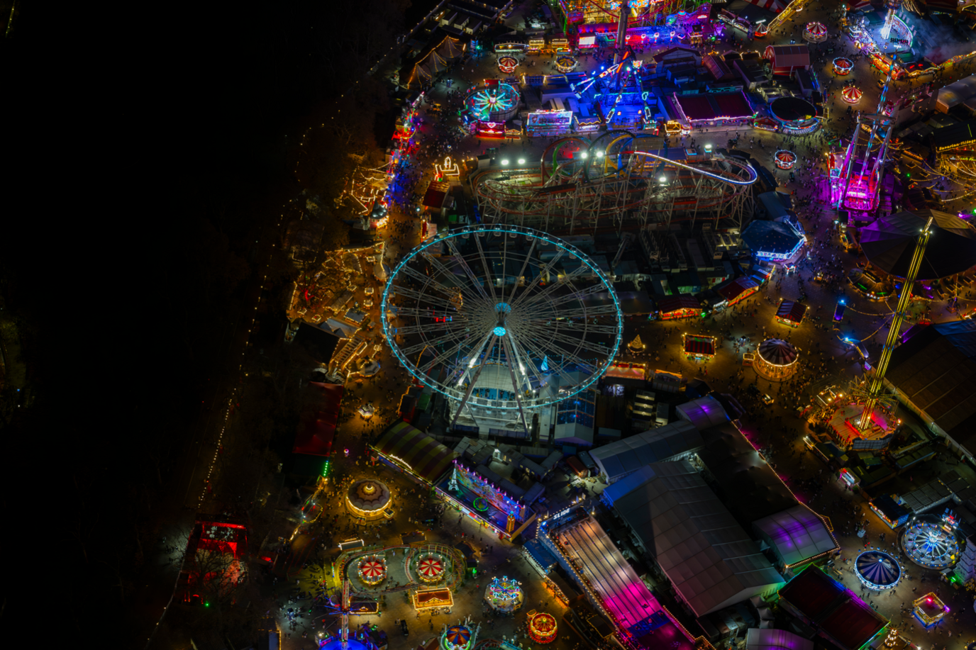 Aerial photograph taken at night showing Ferris wheels, roller coaster and other rides lit up in different colours in Winter Wonderland