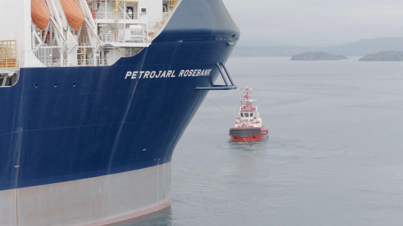 A blue Hull of the Petrojarl Rosebank production vessel being pulled into position by a tug.