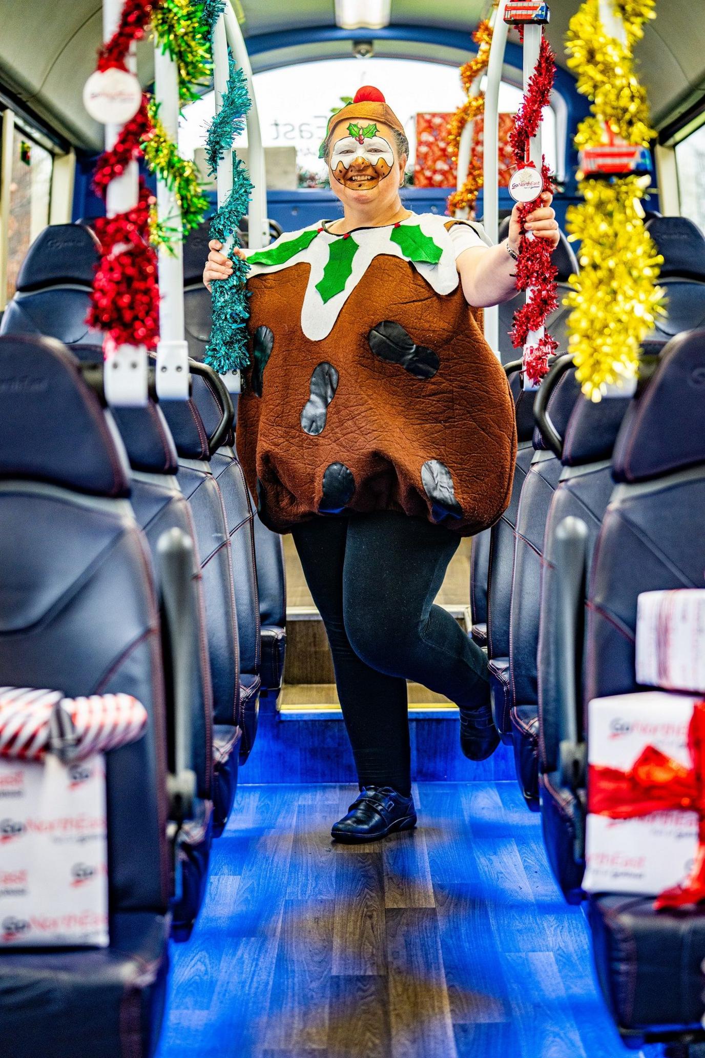 Julie Richardson standing on a bus dressed as a Christmas pudding. She has her face painted.