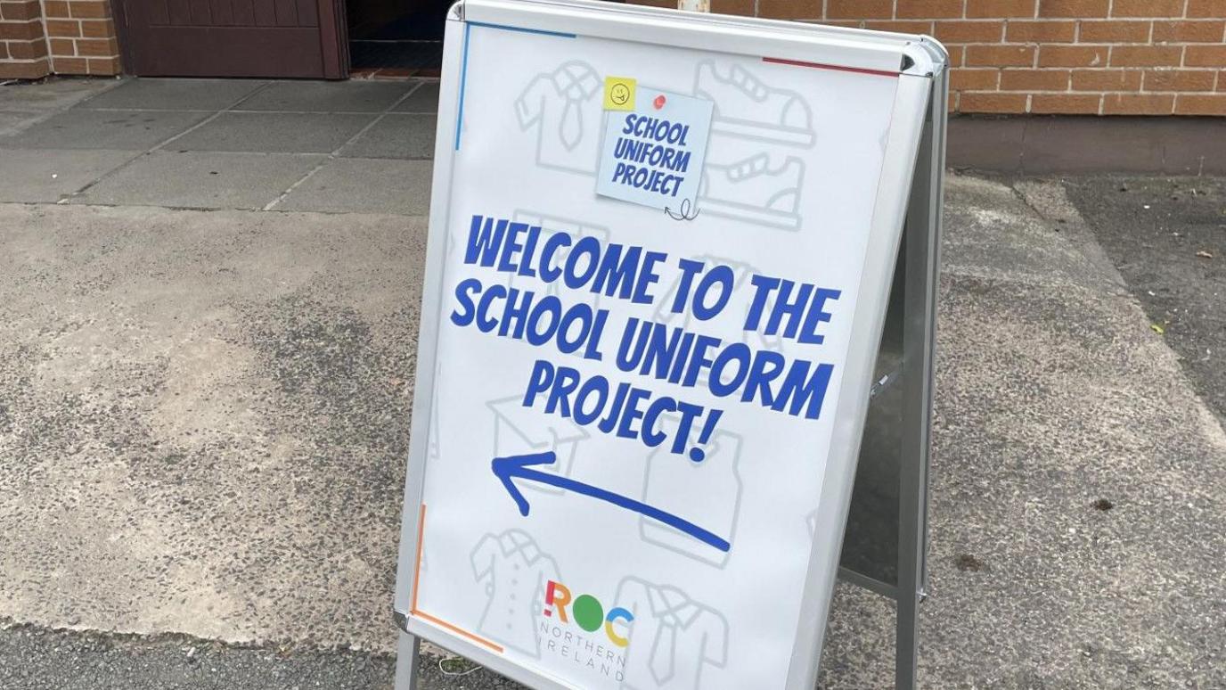 A sandwich board sign which says 'Welcome to the School Uniform Project' in bold, blue letters