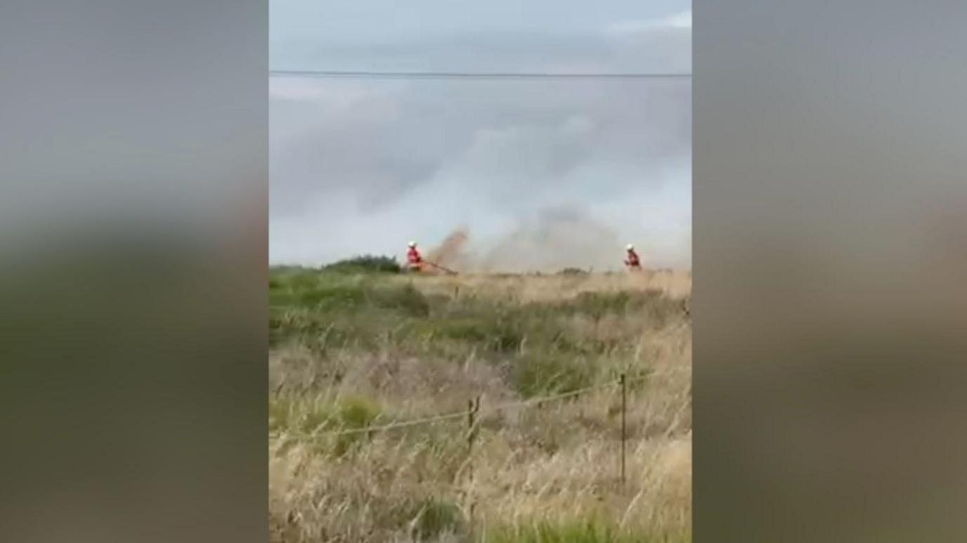 Fire crews in a field in Romney Marsh using high pressure hoses to put out flames