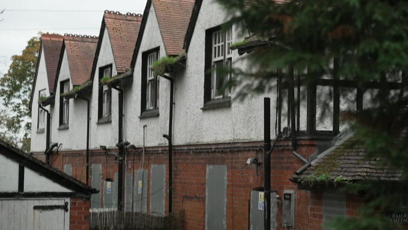 A row of houses is photographed with their doors and windows all boarded up.