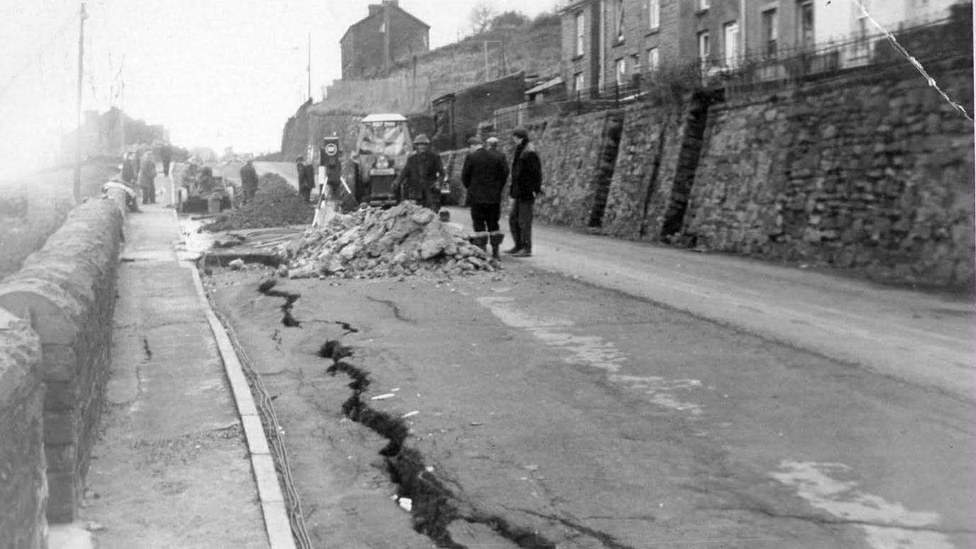 LLun du a Gwyn o Graig Road, y ffordd wedi'i hollti a rwbel ar hyd y ffordd