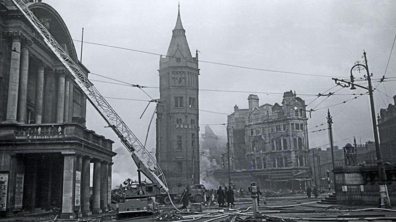 Hull's Queen Victoria Square smoulders after a raid. Firemen's ladders and hoses litter the square.