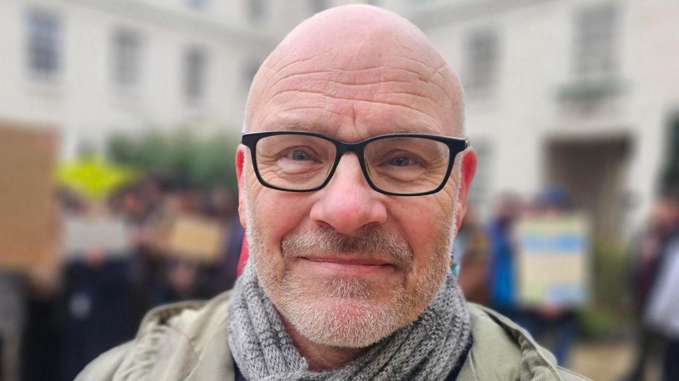 Image of Paul. He has a bald head, grey stubble and is wearing black-framed glasses.