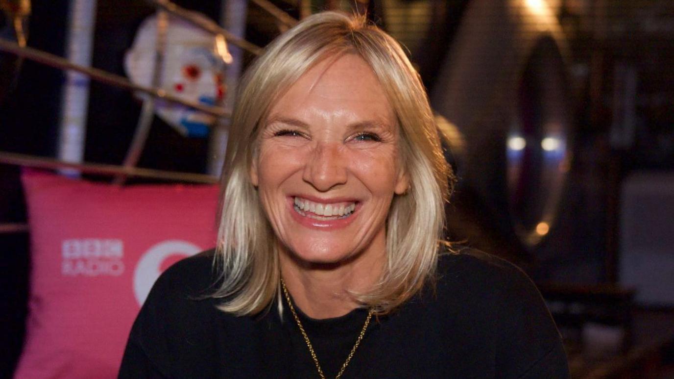 A happy woman smiling at the camera. She is wearing a black top.