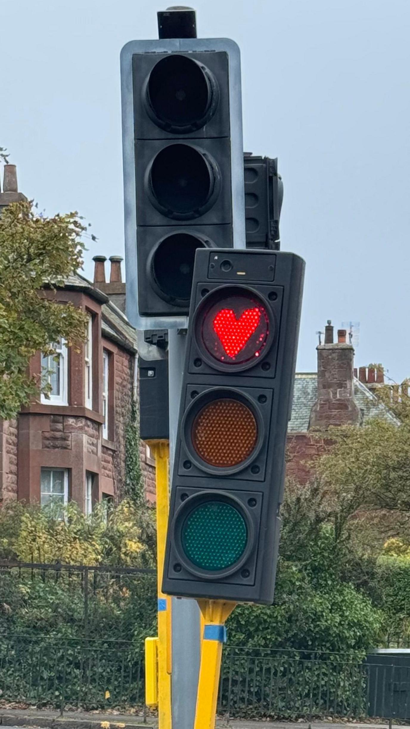 Portrait image showing a temporary traffic light with the red light showing a hand-drawn heart instead of a plain circle