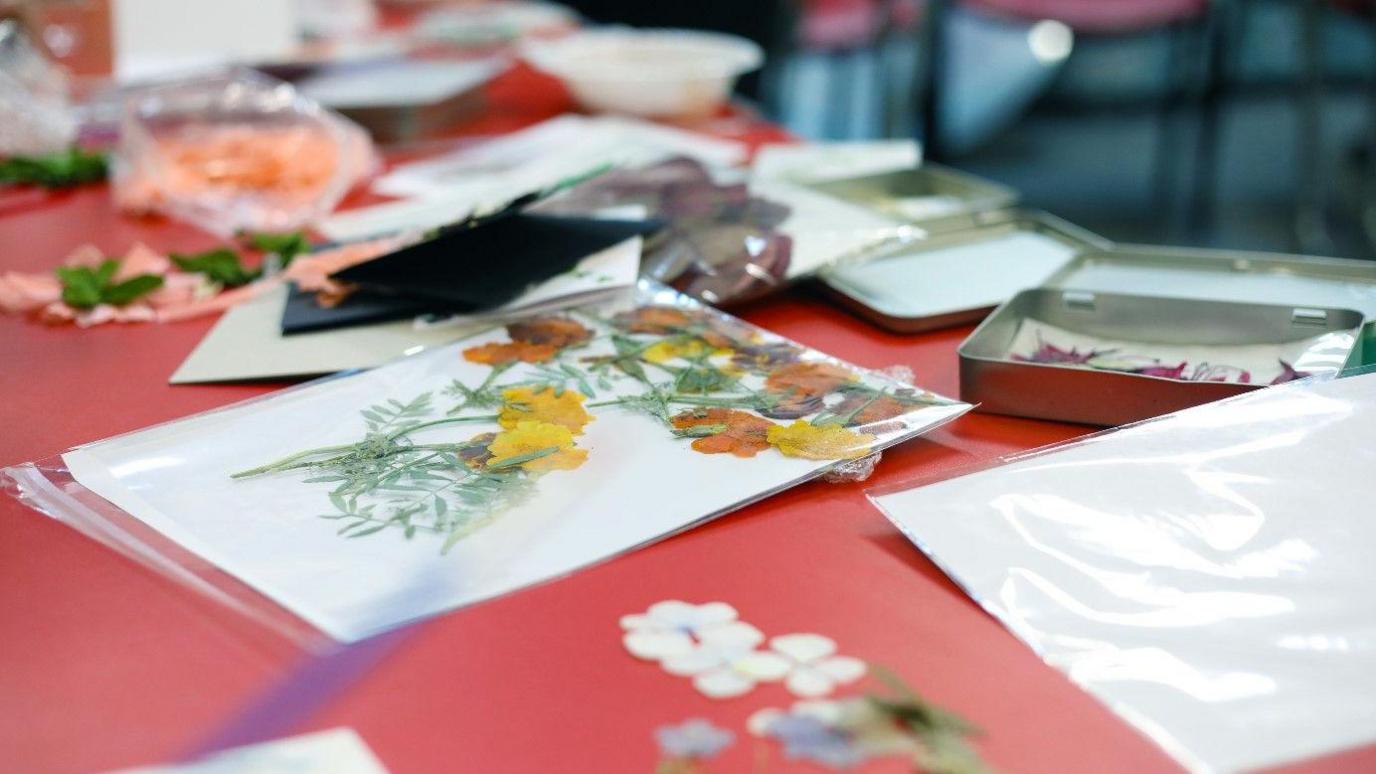 A table with bags of flowers dotted around it, as well as yellow and orange pressed flowers on a piece of white paper. 