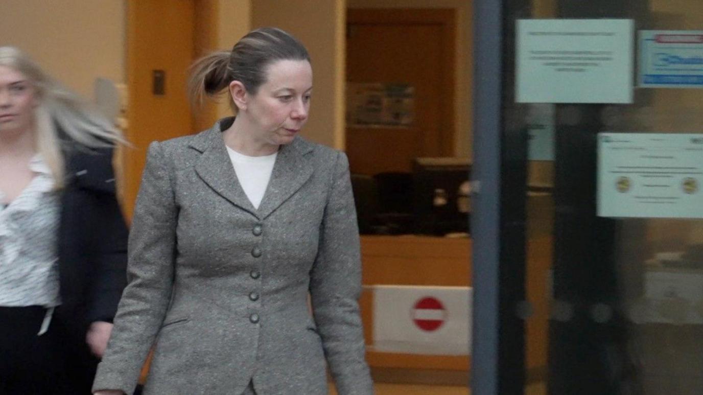 Woman in grey suit and pony tail leaves court building