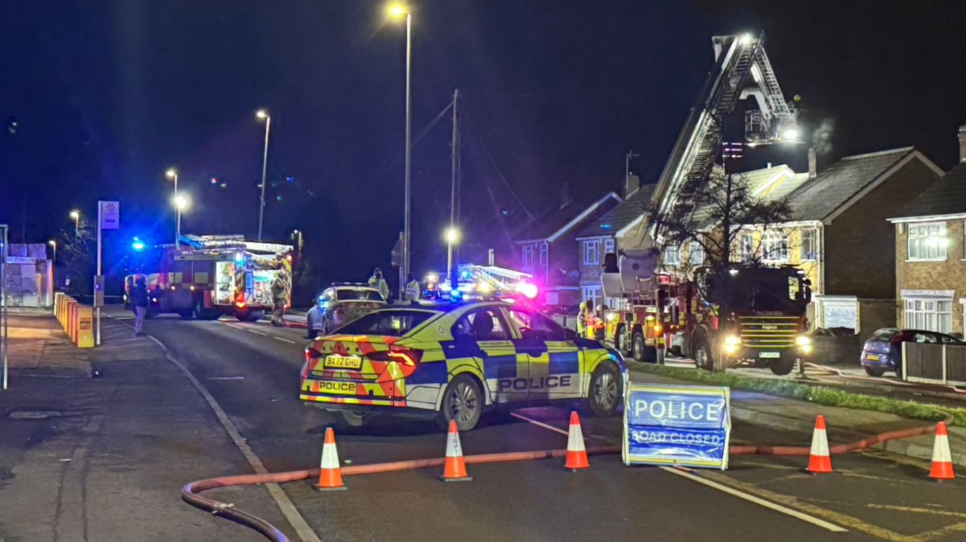 Several emergency service vehicles parked on a road at night with orange cones blocking the street.