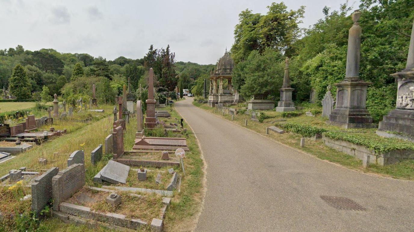 A screenshot from Google showing a path which winds through Arnos Vale Cemetery. The site is very green and surrounded by lots of mature trees. The graves look old, and some have large stone plinths and statues. 