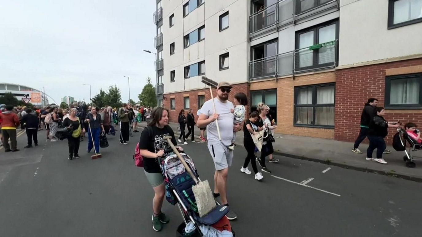 people walking in the street with brooms and cleaning equipment.