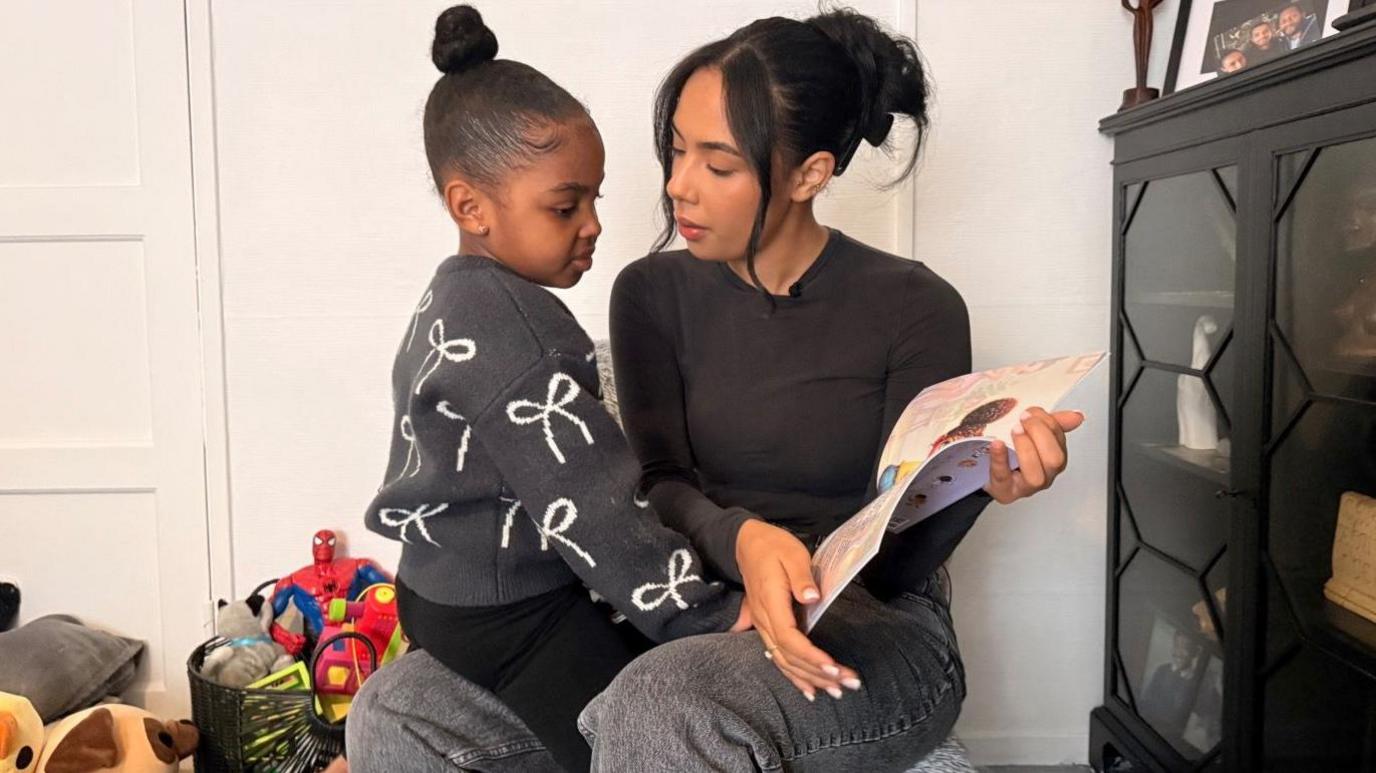 Zaeah's mum reading to her daughter. Zaeah is sat on her lap.