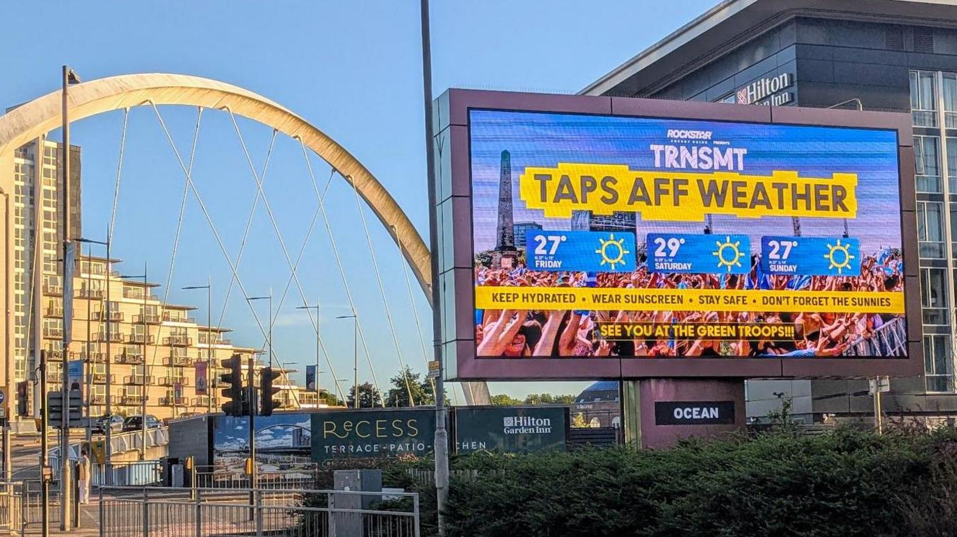A large billboard beside a bridge with temperatures fro trnsmt
