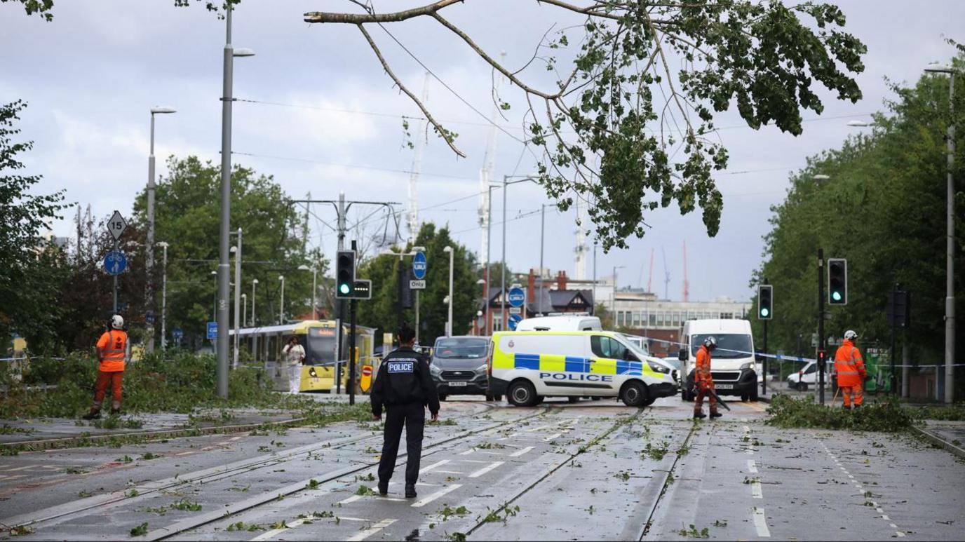 A police officer looks on as workers begin to remove fallen tree branches after strong winds brought by Storm Lilian brought down trees blocking roads and tram routes in Manchester.