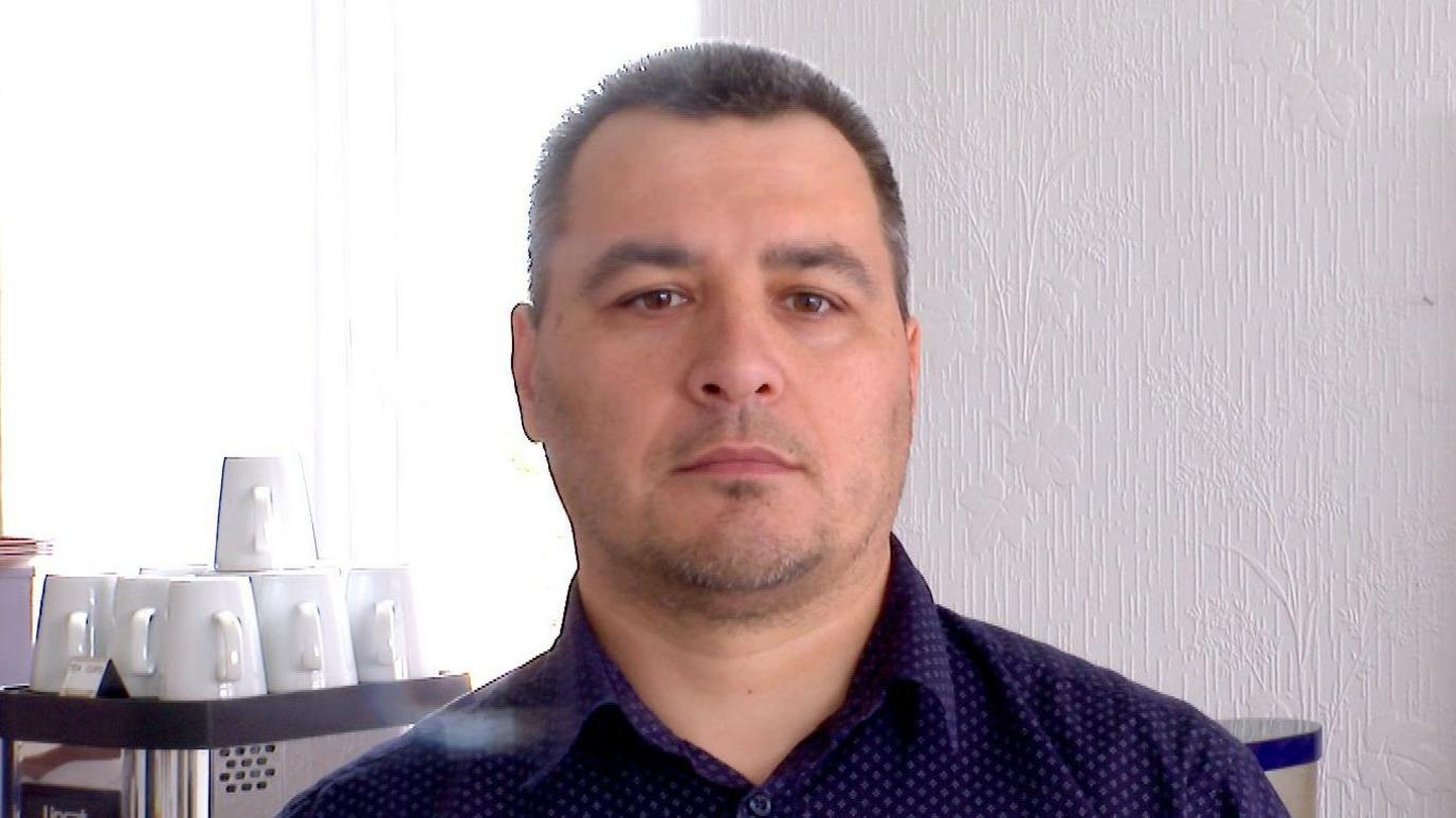 Hotelier Igor Kalinicenko standing in front of a coffee machine in the breakfast room in his hottel