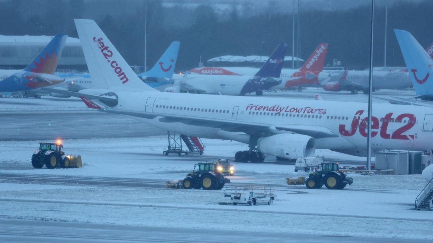 Staff use tractors to help clear snow from around aircraft after overnight snowfall caused the temporary closure of Manchester Airport