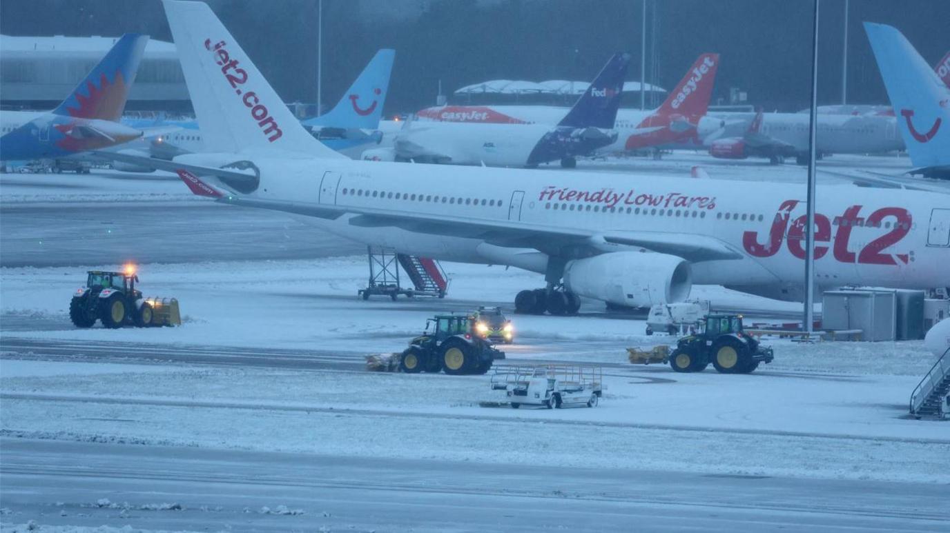 Staff use tractors to help clear snow from around aircraft after overnight snowfall caused the temporary closure of Manchester Airport.