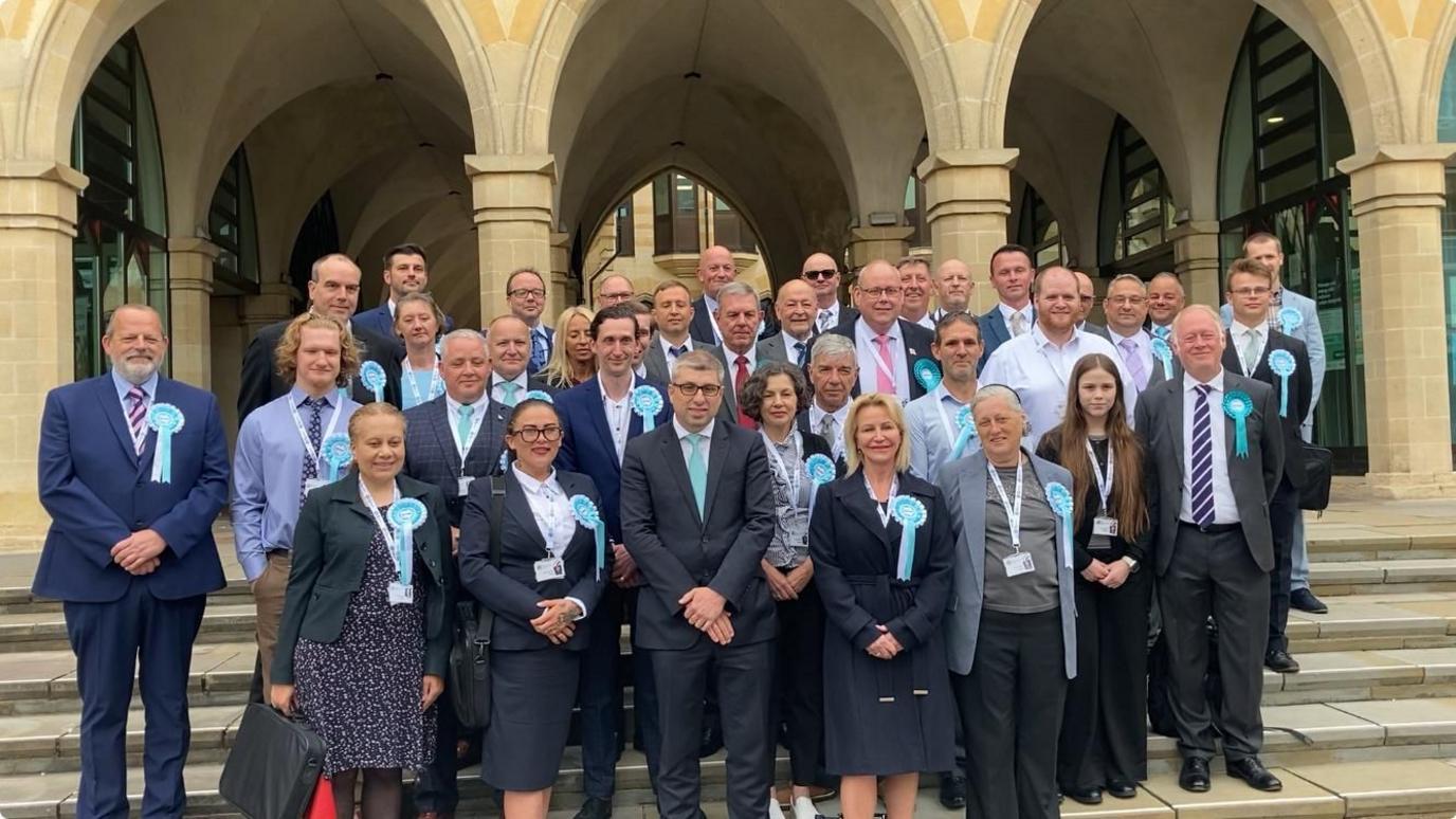 Group of Reform UK councillors most wearing suits and the party rosettes