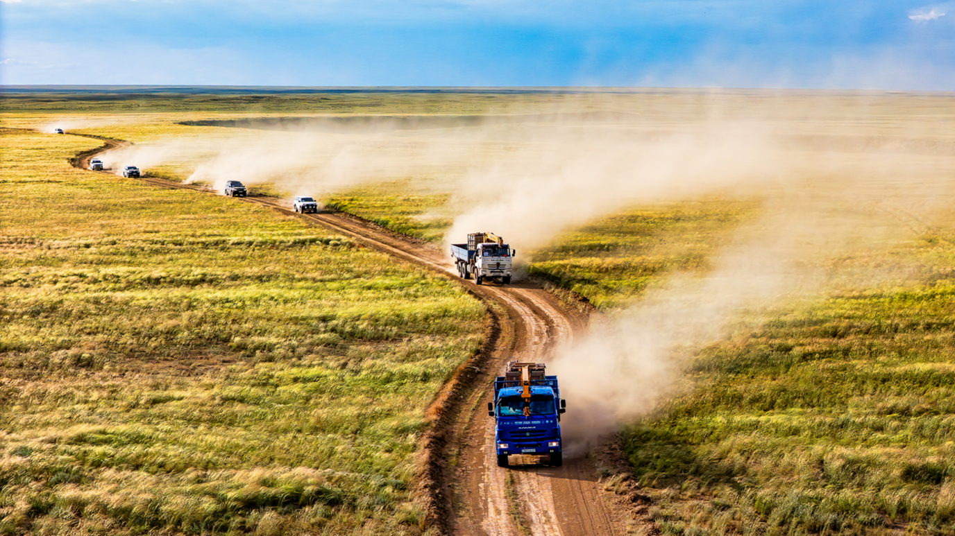 An aerial view of a convoy of lorries following a winding dirt road through a wide, grassy plain