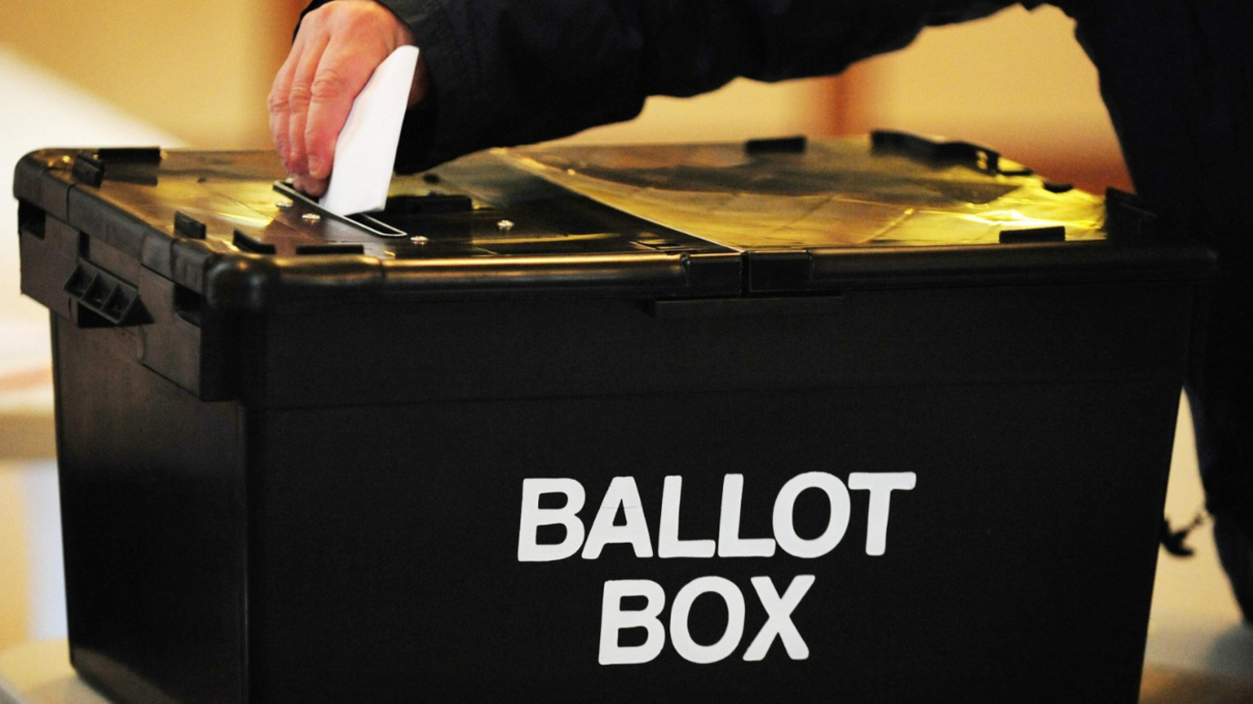 A black box with the words Ballot Box in white and a hand with a card above.