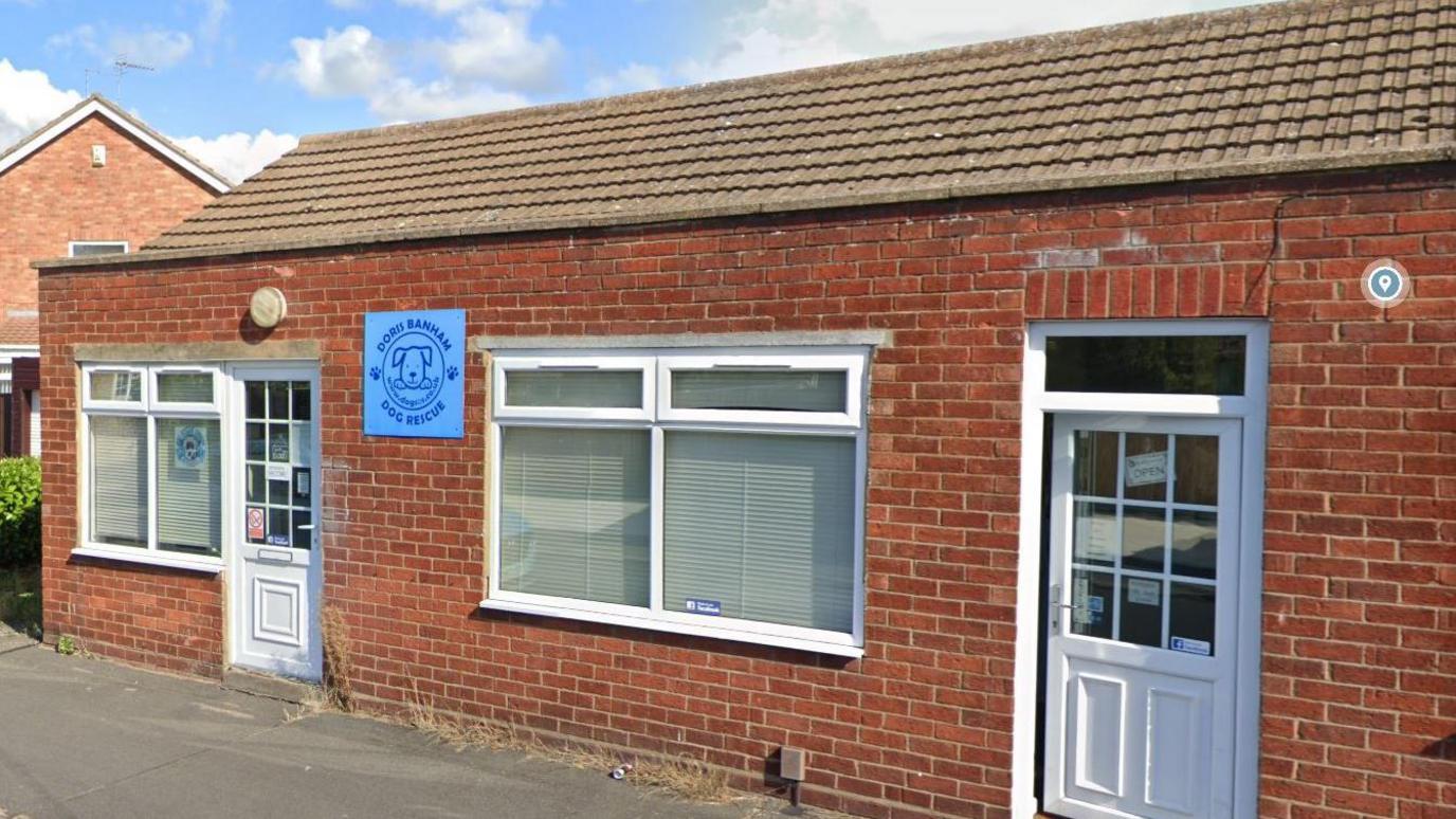 Doris Banham Dog Rescue's charity shop in North Hykeham. It is a small brick-built building with two front windows and a UPVC white door. 