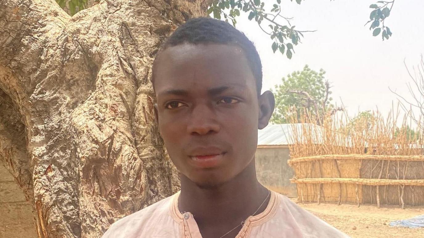Nigerian hunter Abubakar Shehu wearing a pink gown, looking sad
