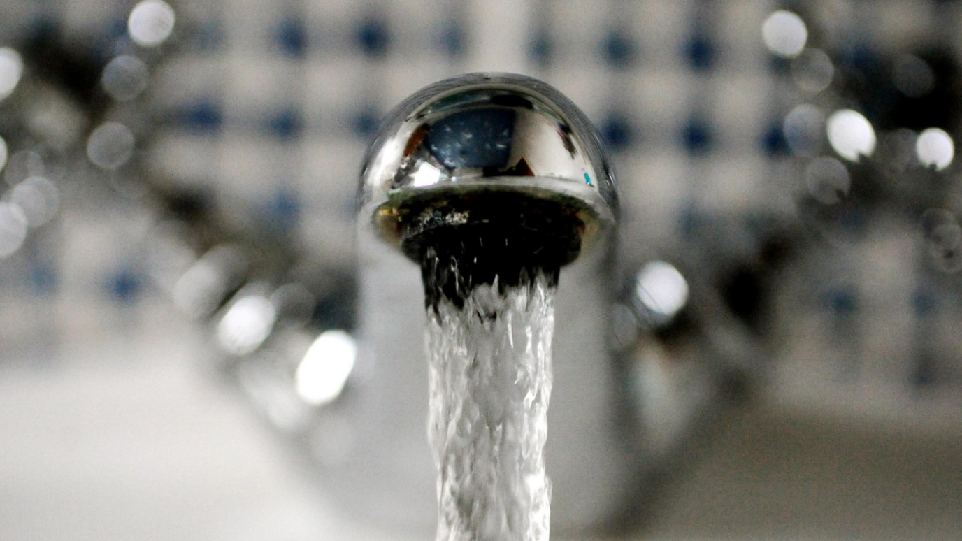 Water runs from a tap, the background is blurred out to focus on the tap