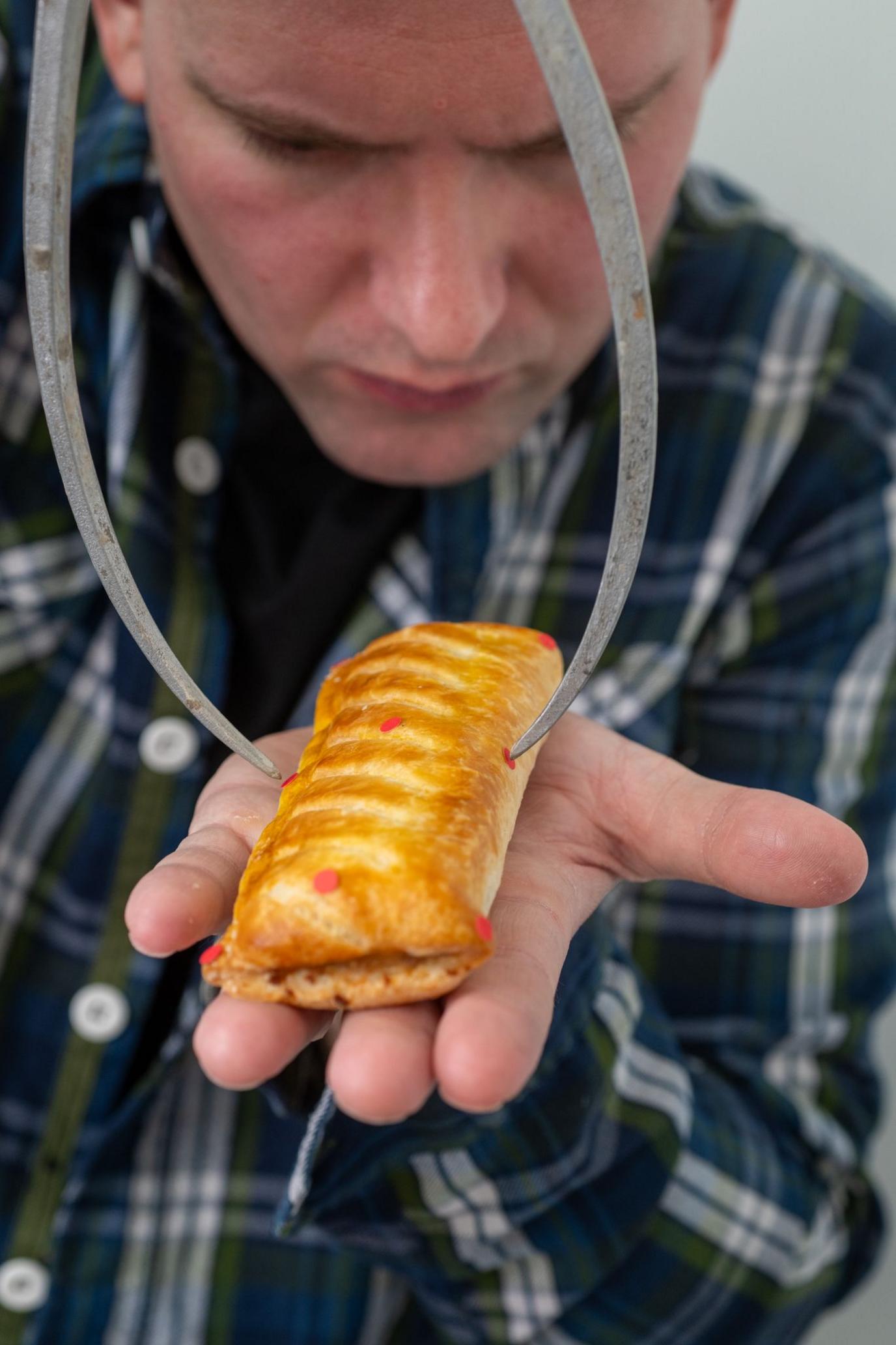 A man measures the dimensions of the sausage roll with a metal tool
